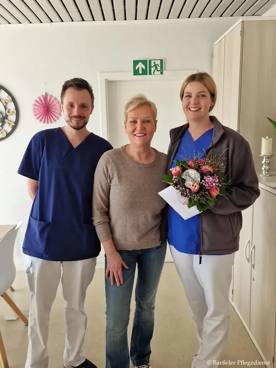 Zwei Pflegekräfte des Barßeler Pflegedienstes mit einer Kollegin, die einen Blumenstrauß hält