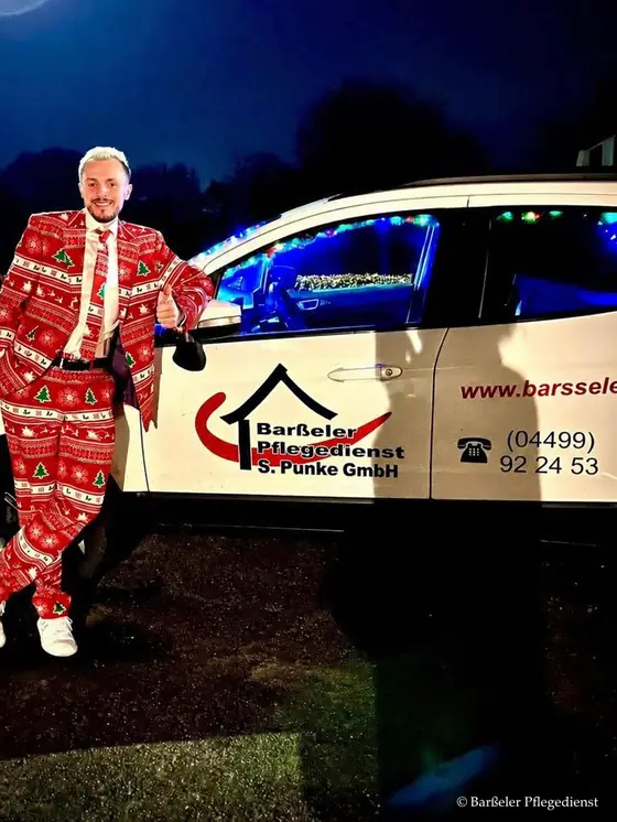 Mitarbeiter im weihnachtlichen Anzug am Abend neben einem Dienstwagen des Barßeler Pflegedienstes